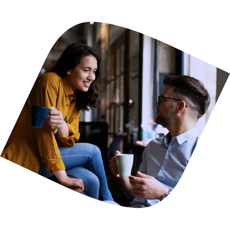 Man and woman sit talking to each other while holding coffee cups