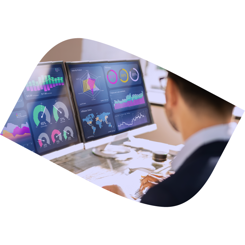 Man types on keyboard with two monitors in front of him displaying charts and data