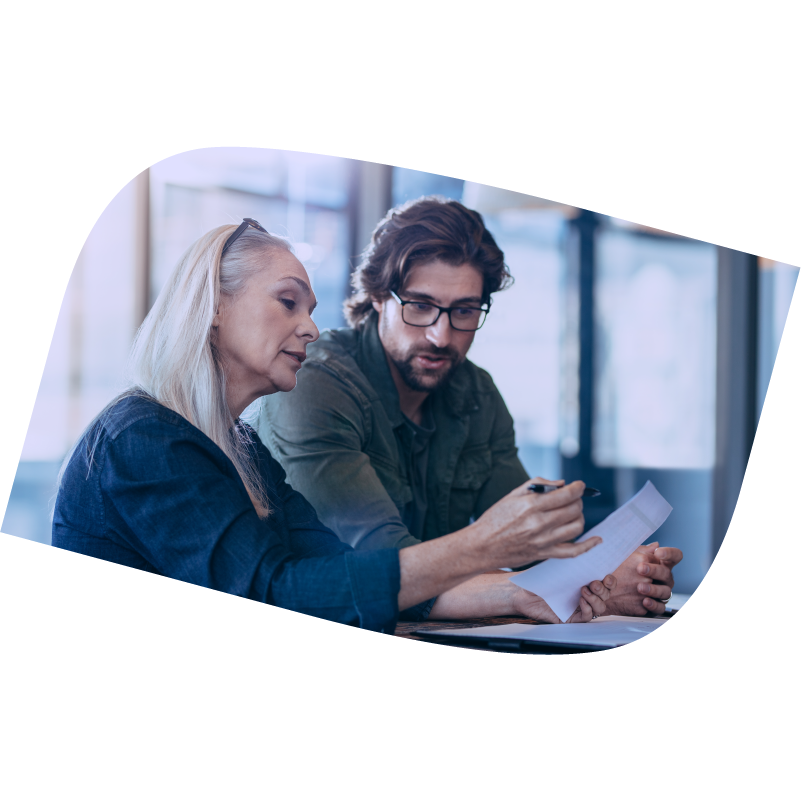 Woman sits and holds paper and pen while man next to her looks on