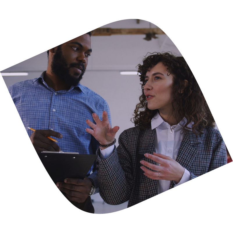 Man holds clipboard and pen in conversation with woman gesturing